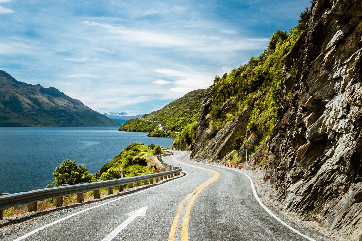 A long windy road with large rock walls the the right and a large vast lake to the left. The image has one of The Photographers Passports Lightroom mobile presets applied to it.