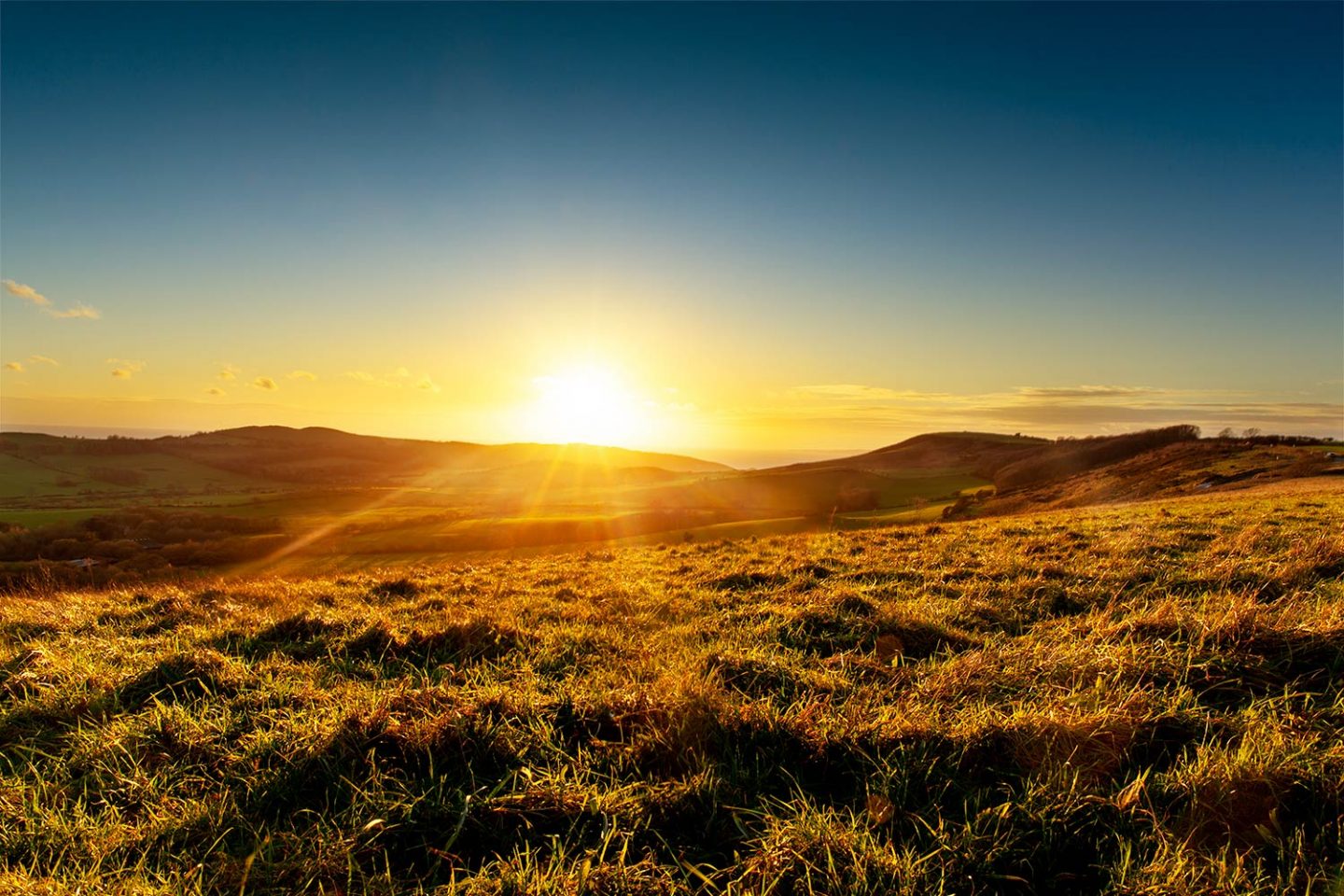 A perfect sunset looking straight towards the setting sun with a large grassy hill that leads towards the sea.