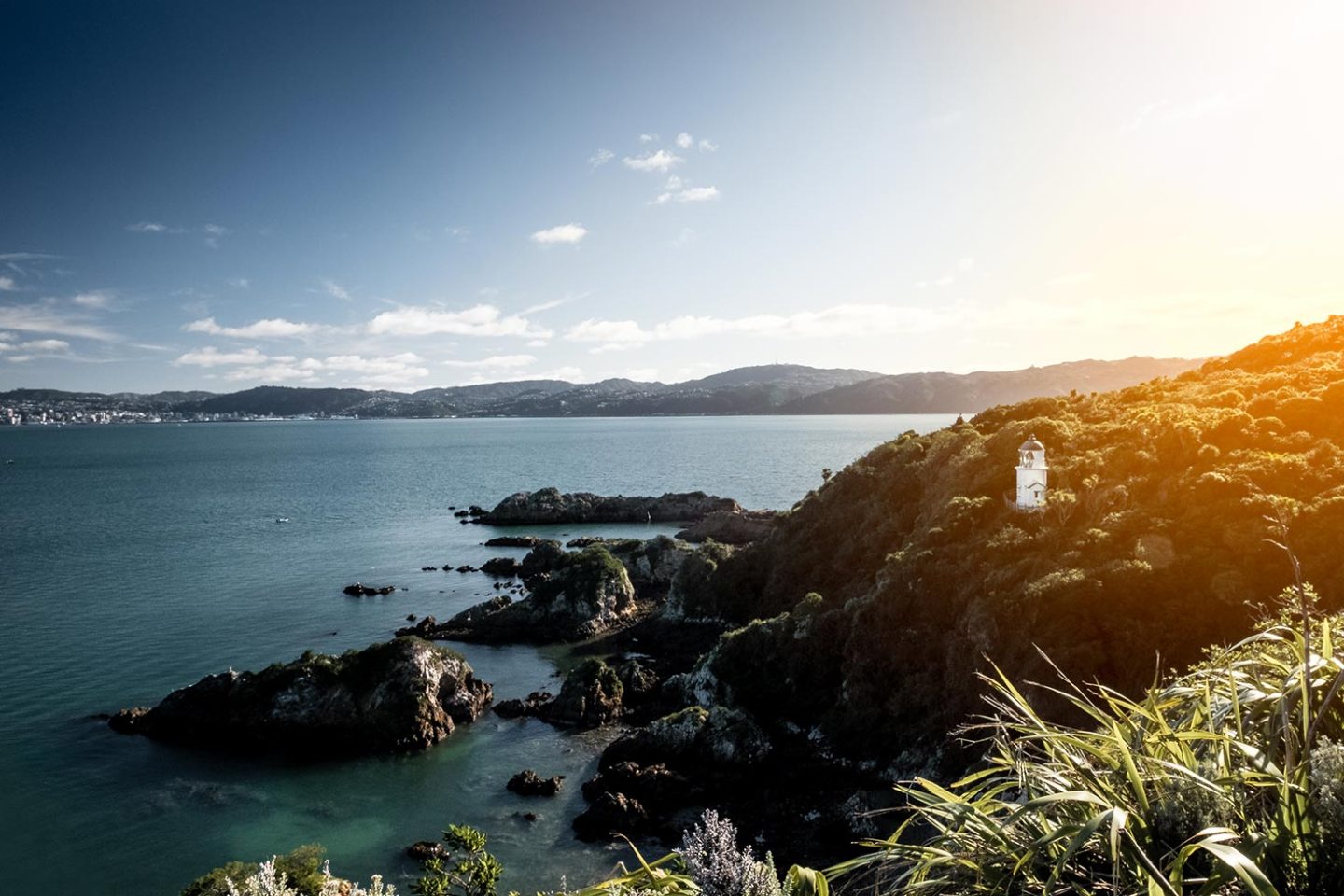 Looking out to sea from an island, in the foreground to the right is a lighthouse on the edge of a cliff.
