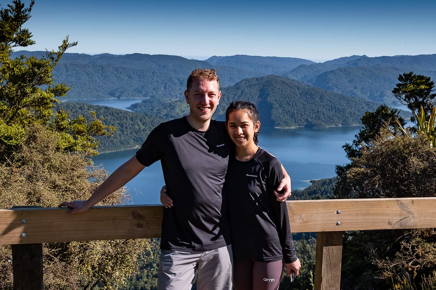 A man and woman photographed with a lake in the background. This photo was taken at Panekire hut on the Lake Waikaremoana Great Walk