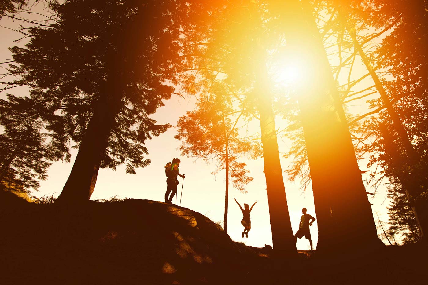 A few friends hiking on a hill with the golden sun behind them. One is jumping in joy.